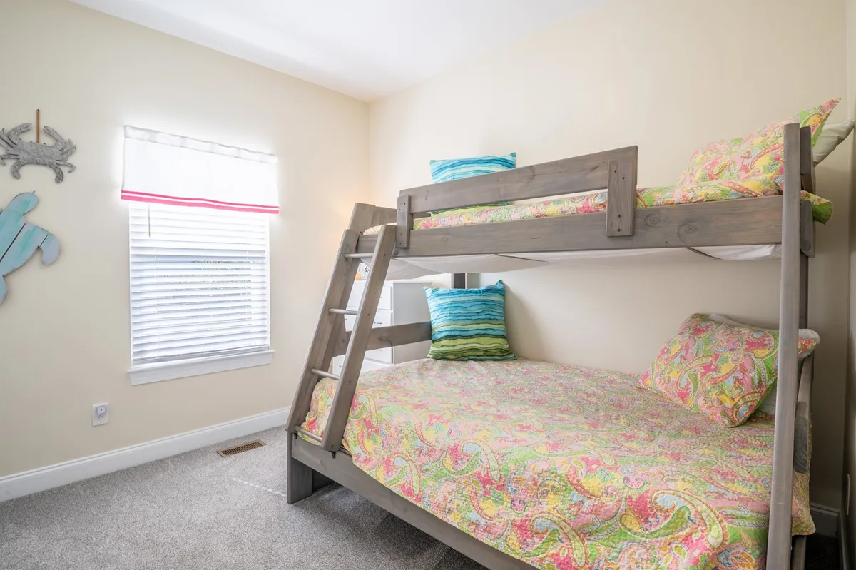 A playful bedroom scene shows a twin-over-full bunk bed with colorful bedding and decorative wall art. The room feels lively yet cozy, clearly designed with children or families in mind, inviting both sleep and imaginative play.