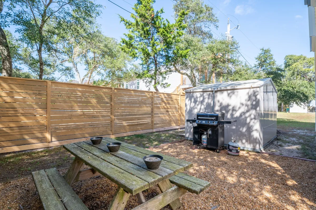 A backyard scene showcasing a picnic table beside a grill, with a wooden fence and storage shed in the background. The setting is relaxed and spacious, ideal for outdoor dining, barbecues, and group activities.