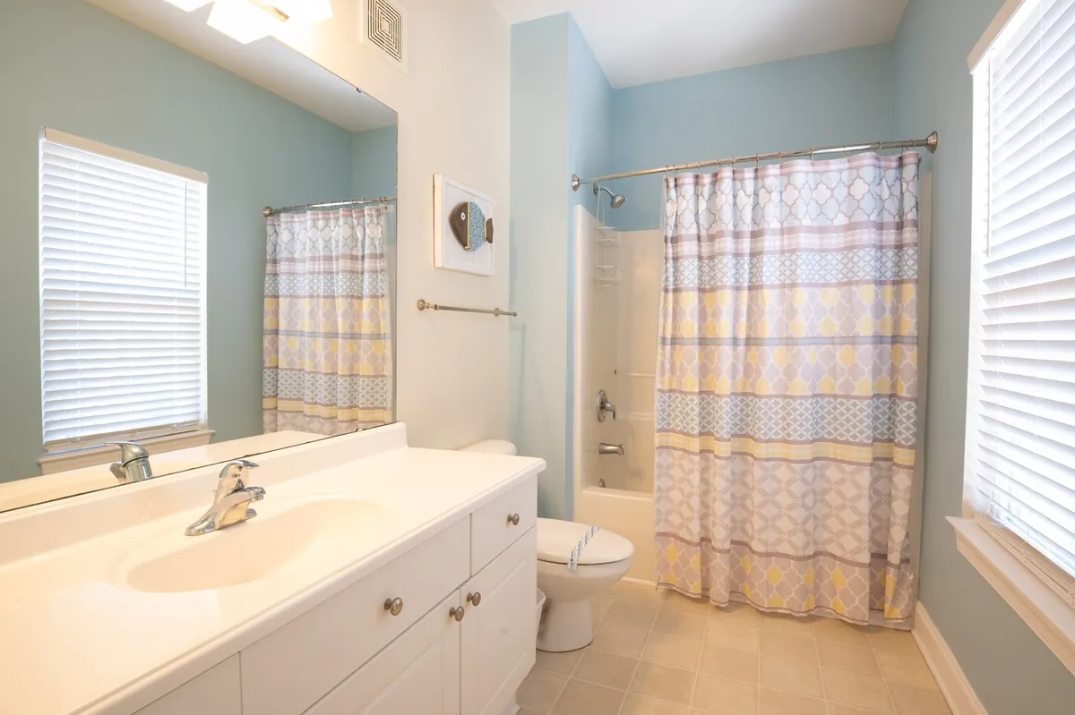 A modern bathroom setting with a vanity sink, a colorful shower curtain, and a large mirror. The space appears fresh and functional, perfect for morning routines or relaxing after a long day.