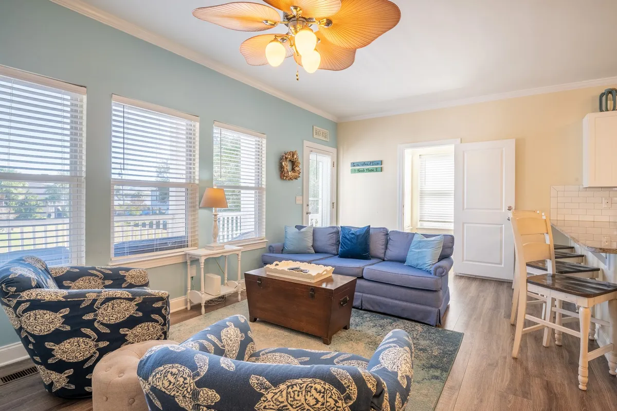 A bright living room with a plush sofa and blue armchairs arranged around a coffee table, bathed in natural light. The scene suggests a comfortable space to relax and recharge after days spent outdoors.