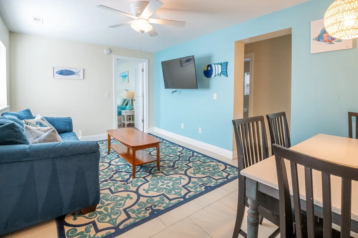 This image captures an open view of the main living area, showing a comfortable sofa, coffee table, dining table, television, and playful decorative fish art. The space is bright and inviting, ideal for both relaxing and gathering. It highlights the seamless flow between the living and dining spaces, central to the section’s emphasis on connection.