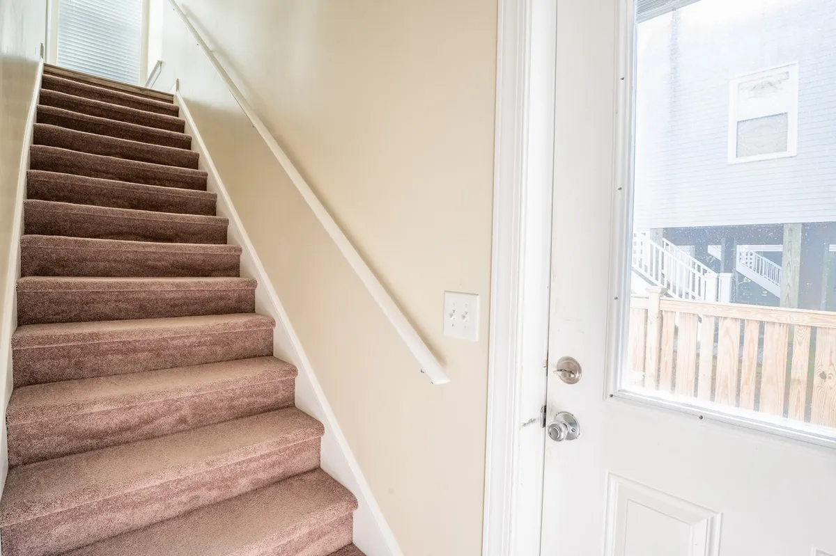 This image shows an inviting staircase leading up to a doorway, with soft carpet and gentle lighting creating a sense of welcome and transition. The view hints at entering or exiting the home, suggesting the connection between the interior retreat and outdoor adventures.