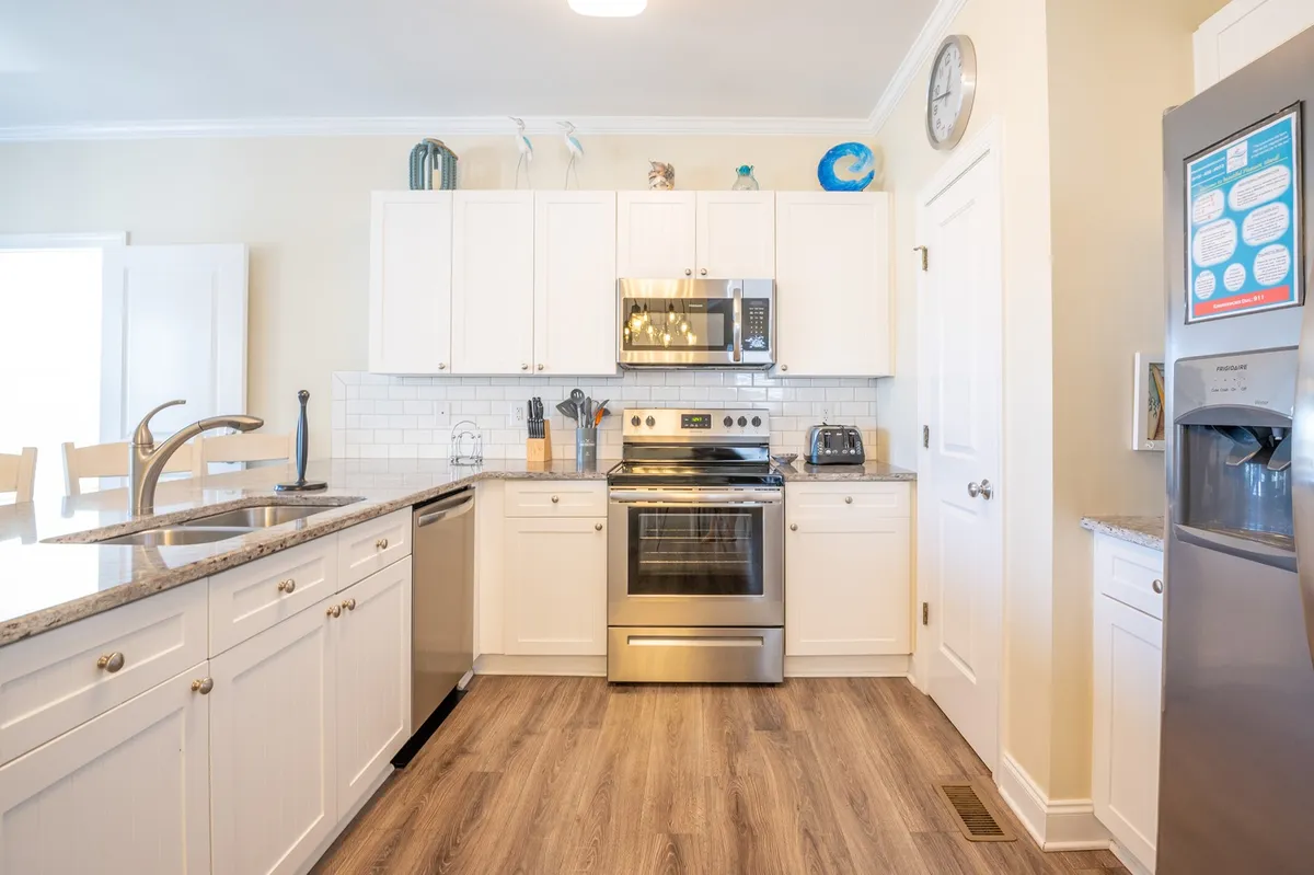 The kitchen is featured here with gleaming stainless steel appliances, granite countertops, and white cabinetry. Decorative items on the top shelf add a personal touch. The setup is bright and organized, with enough space for family cooking and casual breakfasts at the bar.